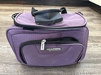 Closed small light purple travel bag with front zippered pocket and handle, showing 'Tracer' logo