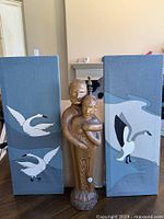 Overall view of hand carved wooden sculpture centered between two painted panels with birds