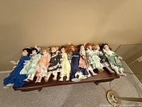Full view of all ten ceramic dolls laid out on wooden table, showcasing their variety in clothing colors and styles.