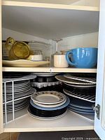 Shelf view of assorted plates, bowls, cups, and crystal items including blue cup and yellow-lid container