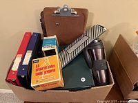 Box of assorted office and school supplies showing binders, clipboards, slide preparation boxes, striped slide holder, and travel mug.