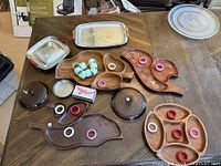 Photo showing assorted wooden divided serving trays, metal baking pans, small ceramic or plastic rings, and lids arranged on a wooden table.