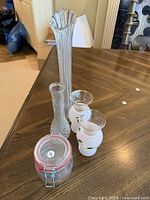 View of assorted glass items on wooden table including vases and storage jar