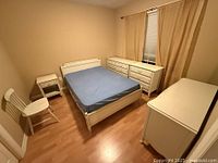 Room view with queen size bed frame, two dressers, and chair arranged in the room.