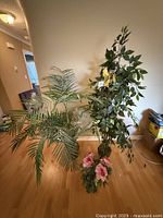 Full view of three artificial plants including two tall plants and one small flower pot arrangement on hardwood floor