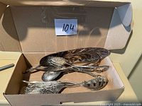 Overview of the four silver serving utensils inside a cardboard box