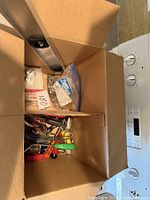 Photo showing an open cardboard box filled with various hand tools including screwdrivers, scissors, and pliers seen from above.