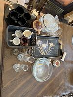 Assorted dishware items including plates, cups, glasses, pitchers, and trays arranged on a table.