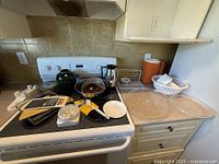 Kitchen countertop and stove with an assortment of kitchen items including kettles, pans, utensils, and serving trays visible