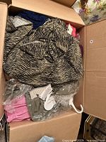 Top view of a box with assorted women’s clothing including a zebra print garment, pink items, and some wrapped pieces.