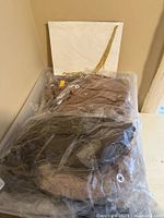 Clear plastic bin with assorted new women's clothing items in original packaging or with tags, primarily beige and black pieces visible.