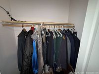 View of closet rod with men's jackets and women's clothing including dresses with tags and packaging
