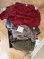 Box of assorted new clothing items in soft fabric, colors include red, olive, beige, cream with tags visible