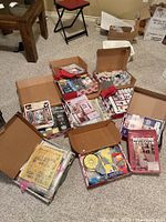 Six open boxes containing a mixture of painting supplies: paints, brushes, kits, manuals, and craft materials spread on carpeted floor.