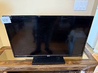 Front view of the RCA flat screen TV on a wooden table, screen off, showing the black bezel and base stand.