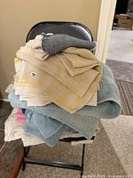 Stack of assorted used tea, hand, and bath towels folded and placed on a folding chair indoors.