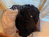 Large bin filled with folded used clothing items including black, beige, and striped fabrics.