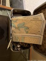 Opened vintage box showing folded nautical charts inside along with cords and miscellaneous small items