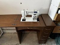 View of full sewing table with sewing machine built in, showing drawers, handle, and flat surface.