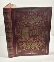 Photo of front cover of the antique book showing red leather cover with gilt title and decorations.