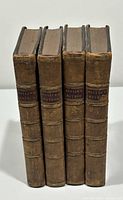 Four leather-bound volumes upright, spines facing forward showing gilt title labels