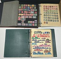 Four binders open showing pages of world stamps mounted on black and cream colored pages with protective sheets.