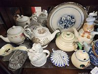 Front view showing the 15-piece assortment of teapots, creamers, decorative plates, and other ceramics in various styles and decorative motifs including floral, animals, and stripes.