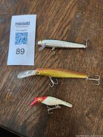 Photo of three fishing lures on wood floor with lot number card, showing all lures laid out