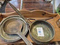 Three metal frying pans including a copper pan with patina, shown stacked with visible wear and use.