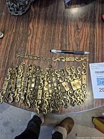 40 brass drawer front handles spread out on wooden surface next to a ballpoint pen for size reference.