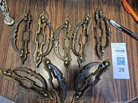 Eight ornate brass drawer handles arranged on a wooden surface.