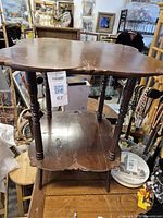 Antique wooden side table with scalloped edges on top and lower shelf, spindle legs, showing signs of wear and age.
