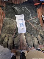 Pair of black leather welding gloves laid palm side up on a wooden surface, showing signs of wear and some discoloration.