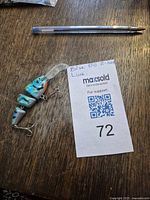 Full view of blue segmented minnow fishing lure with pen for scale and auction tag
