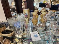 Lot contents on a glass shelf displaying various glassware, including swirled vases, clear glasses, blue and white ceramic/glass items, and a covered sugar bowl.
