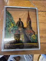 Full view of the glass framed painting showing Aachen Cathedral with detailed architecture and greenery, glass frame with metal edges and hanging chain