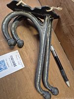 Two large cast iron wall hooks shown with decorative curved double hooks and scalloped mounting plates with holes for wall mounting. Shows condition and size relative to pen.