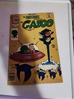 Full front cover of the comic book showing The Great Gazoo flying with Fred Flintstone and traffic light with birds.
