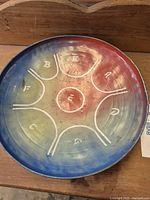 Top photo shows circular metal drum face with eight tone tongues marked with white numbers and letters from 1 to 8 and a central 'C' on a rainbow gradient surface.