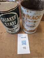 Two vintage motor oil cans side by side, one Texaco can without lid, one Quaker State can with lid.