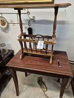 Two photos showing a wooden magazine table with turned legs, lower spindled magazine rack, and rectangular top surface. It is placed on another wooden side table with a simple design and rectangular top. The photo highlights the two wooden tables stacked.