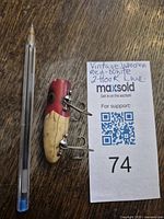 Photo showing vintage wooden fishing lure alongside a pen for size comparison.