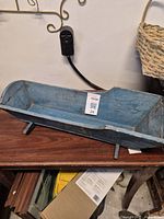 Side view of the wooden blue doll cradle on a wooden surface, showing the front and side shape.