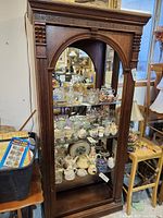 Front view of the wooden display shelf showing carved arch and glass shelves with various items inside.