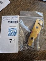 Wooden yellow spotted fishing lure with two attached rusty treble hooks inside a plastic bag, alongside a MaxSold auction lot tag.