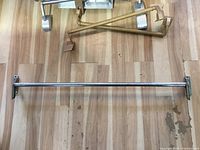 Chrome hanging rod laid out on wooden floor, showing full length and mounting brackets.