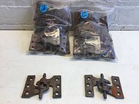 Two sealed plastic bags containing multiple left and right metal hinges clearly labeled 'Lft' and 'Rht' alongside one left and one right hinge outside the bags for display, showing metal construction with mounting holes and pivot design.