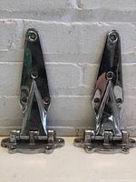 Front view of a pair of antique chrome refrigerator hinges showing polished chrome finish and three mounting holes on the upper and lower plate, along with pivot mechanism.