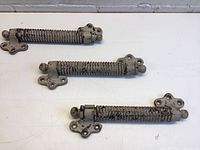 Three antique metal springs approximately 10 inches long with mounting brackets and spherical ends placed on a white surface.