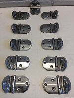 Top-down view of 11 chrome Art Deco hinges arranged in rows.